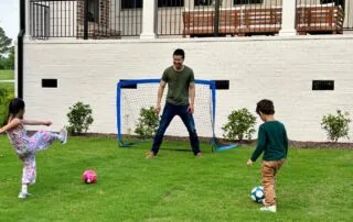 A family playing soccer on a green lawn with an adult and two children