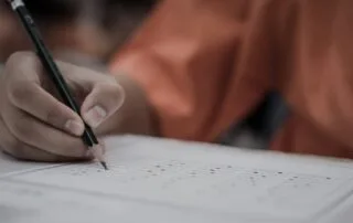 Hand holding pencil over standardized test sheet