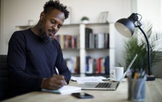 Person studying at a well-lit desk with a laptop, notebook, and coffee mug.