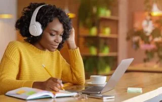 Person wearing headphones and taking notes in a cozy setting