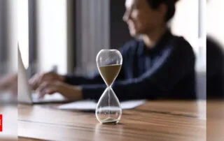 Hourglass and laptop on wooden table representing time management and productivity