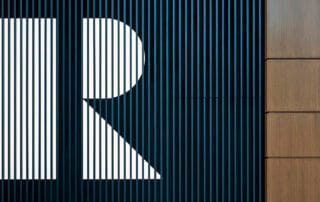 Abstract architectural wall with vertical black slats forming a stylized white “r” next to wood panels