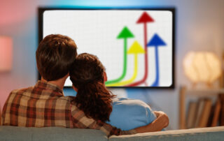 Couple sitting on a couch watching a tv screen displaying colorful upward arrows.