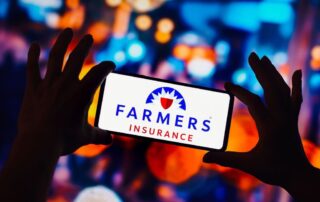 Hands holding a smartphone displaying the farmers insurance logo on a bright blurred background