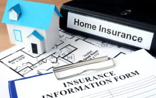 Paper house model, floor plan and documents labeled “home insurance” and “insurance information form” on a desk.