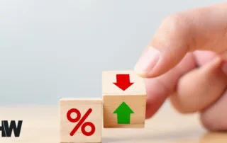 Wooden blocks with interest rate percentage symbol and green up arrow/red down arrow being moved by a hand.
