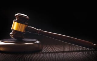 Wooden judge’s gavel resting on a sound block on a dark wooden table, lit against a black background