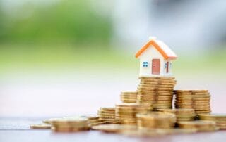 Small model house sitting on top of stacked gold coins representing real estate investment and savings