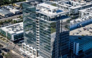 Aerial view of a modern glass high‑rise office building with rooftop terrace and surrounding urban neighborhood.