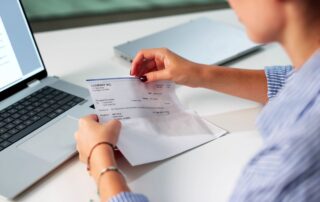 Person opening a paycheck envelope while sitting at a desk with a laptop