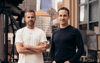Two men standing side by side on an urban rooftop with city buildings in the background