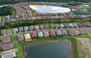 Aerial view of a suburban neighborhood with rows of single-family homes surrounding a central lake and green spaces.