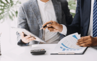 Business professionals reviewing financial charts on a tablet and printed report at a desk.