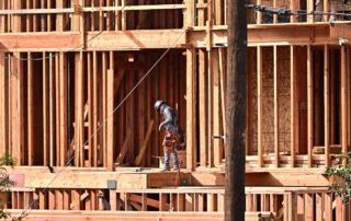 Construction worker standing on wooden framing of a multi‑story building under construction.