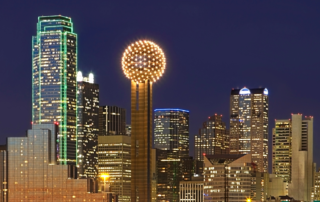 Dallas skyline at night with reunion tower lit up against a dark blue sky