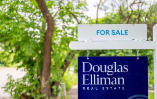 The Housing Market Hits A Winter Chill 7 Real estate for sale sign for douglas elliman in front of leafy green trees.