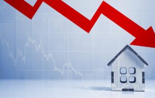 Red downward arrow over a small house model symbolizing a drop in real estate market values.