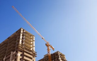 Construction crane beside partially built high-rise buildings against a clear blue sky