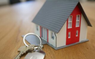 Miniature house model with a keyring and house keys on a wooden table.