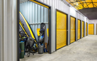 Indoor self storage units with yellow roll-up doors, one open showing recreational gear and equipment stored inside