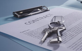 Keys on a keyring lying on top of a signed contract document on a clipboard.