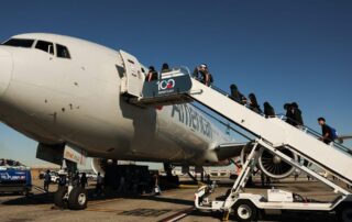 Passengers boarding a commercial airplane via an outdoor stairway at an airport under a clear blue sky.