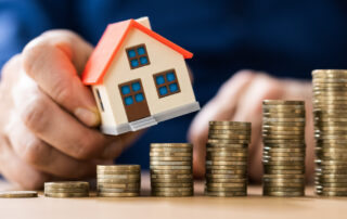 Hand holding small model house above stacked coins representing real estate investment and property value growth