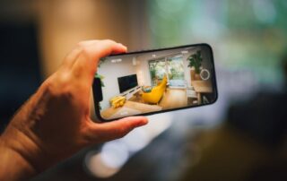 Person holding a smartphone taking a photo of a modern living room with a yellow armchair and large glass doors.