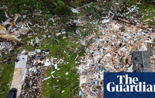 Zillow Drops Climate Risk Scores—What It Means For Agents, Buyers, And The Future Of Real Estate 5 Aerial view of a destroyed neighborhood with houses reduced to scattered debris across a green landscape.