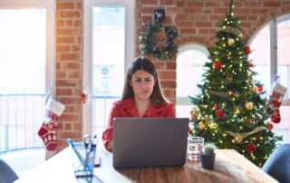 December Mortgage Outlook: Why Rates May Rise Despite Market Confusion 6 Woman working on a laptop and looking frustrated in a home office decorated for christmas with a lit tree and stockings in the background