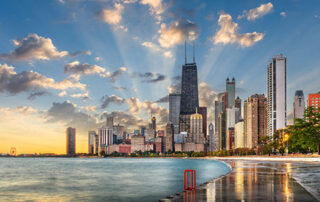 Sunrise over a modern lakeside city skyline with tall buildings and a reflective waterfront path