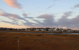 Sunset over coastal marshland with a distant town and pastel clouds in the sky