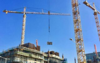 High-rise building under construction with multiple yellow tower cranes against a clear blue sky