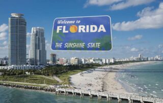 Florida’s Insurance Market Finally Stabilizes After Years Of Crisis, Says State Commissioner 2 Welcome to florida sign over a sunny miami beach shoreline with high-rise buildings, pier, and ocean waves.