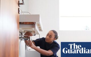 Young plumber in navy workwear fixing pipes beneath a bathroom sink.