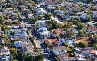 Aerial view of a colorful suburban neighborhood with tree‑lined streets and closely packed houses.