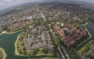 Aerial view of a suburban neighborhood with rows of houses, tree-lined streets, and surrounding lakes.