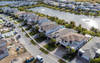 Aerial view of a modern suburban neighborhood with waterfront homes, manicured lawns, and a small lake with fountains.