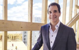 Smiling man in a suit standing inside a wood-framed building under construction