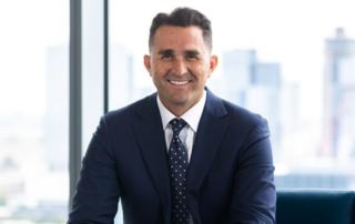 Business professional in a navy suit smiling while seated in a modern office with city skyline in the background