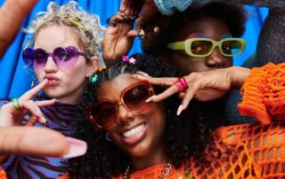 Colorful friends posing playfully in bold sunglasses against a bright blue background