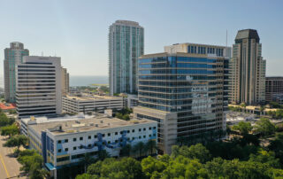 Aerial view of a modern downtown skyline with mid- and high-rise office and residential buildings surrounded by trees near the waterfront.