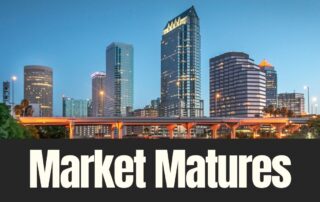 Skyline of modern city skyscrapers at dusk above an elevated highway with the words “market matures” in bold text.