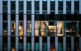 Modern glass office building at night with illuminated empty workspaces visible through the windows