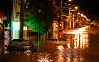 Nighttime street flooding with partially submerged cars and reflections of streetlights in the water.