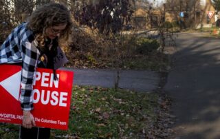 Person placing a red open house sign in the grass beside a residential street.