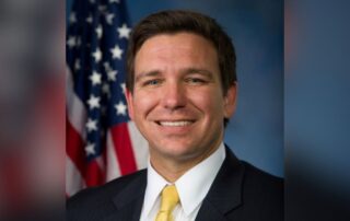 Smiling man in a suit and yellow tie in front of an american flag