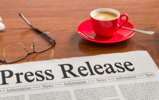 Press release newspaper on wooden desk with eyeglasses, red coffee cup and keyboard