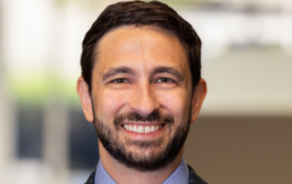 Smiling bearded man in a suit and tie, shown in a professional headshot.