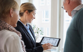 Real estate agent showing an elderly couple a digital floor plan on a tablet in a bright apartment.